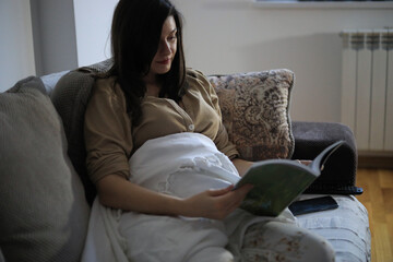 A young pregnant woman is reading a book.
Pregnant woman relaxing with the book.