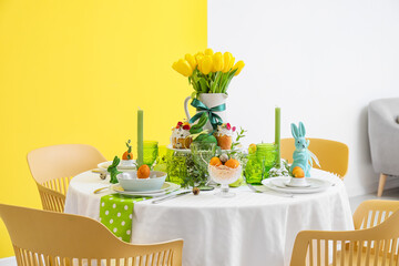 Dining table with stylish dishware, Easter cakes and eggs near color wall