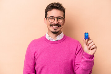 Young caucasian man holding batteries isolated on beige background happy, smiling and cheerful.