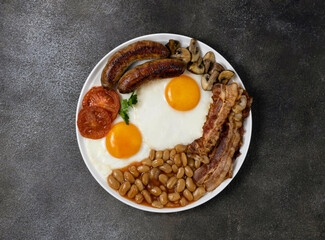 English breakfast with sausages, beans, fried eggs, mushrooms and tomatoes on a dark background, close-up