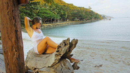 The sexy vibrant young lady is posing on a tree. The woman is having fun on an island vacation. The licentious woman provocative fervently twists her buttocks.