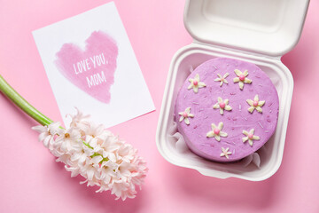 Plastic lunch box with tasty bento cake, greeting card and flowers on pink background