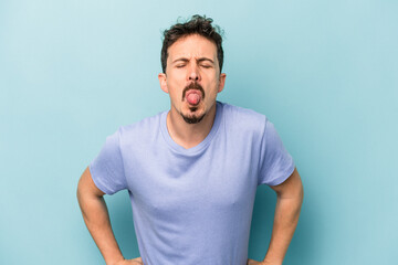 Obraz premium Young caucasian man isolated on blue background funny and friendly sticking out tongue.