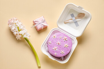 Obraz na płótnie Canvas Plastic lunch box with tasty bento cake, gift and flowers on beige background