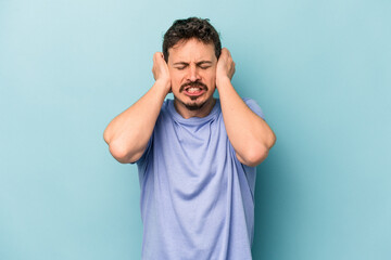 Young caucasian man isolated on blue background covering ears with hands.