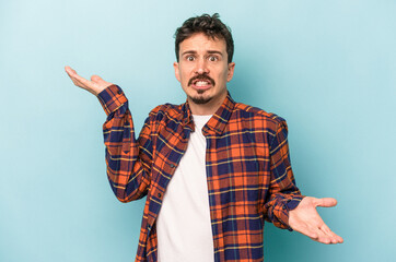 Young caucasian man isolated on blue background confused and doubtful shrugging shoulders to hold a...