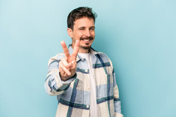 Young caucasian man isolated on blue background joyful and carefree showing a peace symbol with...