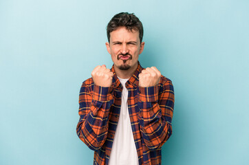 Young caucasian man isolated on blue background showing fist to camera, aggressive facial expression.