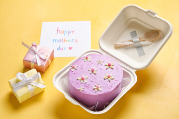 Obraz na płótnie Canvas Plastic lunch box with tasty bento cake, greeting card and gifts on orange background