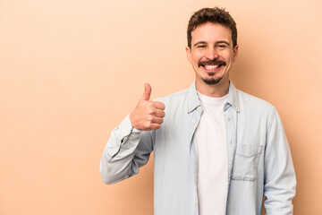 Young caucasian man isolated on beige background smiling and raising thumb up