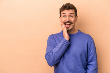 Young caucasian man isolated on beige background shouts loud, keeps eyes opened and hands tense.