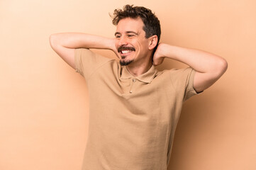 Young caucasian man isolated on beige background feeling confident, with hands behind the head.