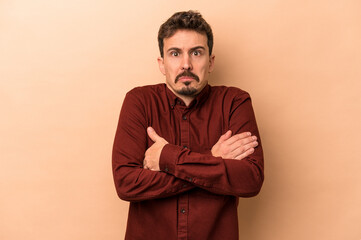 Young caucasian man isolated on beige background shrugs shoulders and open eyes confused.