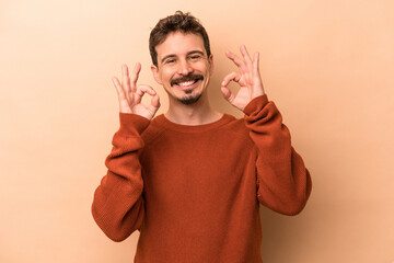 Young caucasian man isolated on beige background cheerful and confident showing ok gesture.