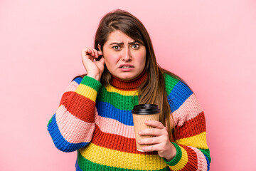Young caucasian overweight woman holding takeaway coffee isolated on pink background covering ears with hands.
