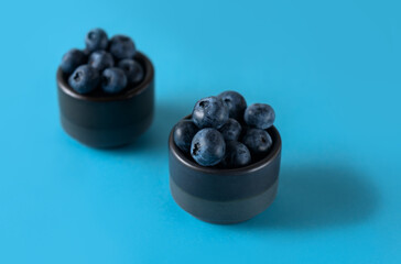 Fresh organic blueberries in two ceramic bowls on a blue background