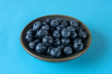 Fresh organic blueberries in a ceramic saucer on a blue background