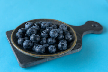Fresh organic blueberries in a ceramic saucer on a ceramic board on a blue background