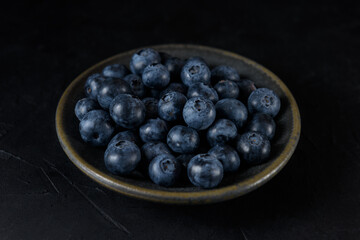 Fresh organic blueberries in a ceramic saucer on a black background