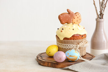 Wooden board with tasty Easter cake and painted eggs on light background