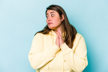 Young caucasian overweight woman isolated on blue background praying, showing devotion, religious person looking for divine inspiration.