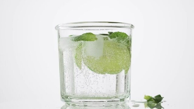 Soda water with lime, mint and ice in the glass on the white background, rotate, 4k. Fresh lime detox water with bubbles.