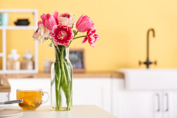 Vase with flowers and cup of tea on dining table in kitchen