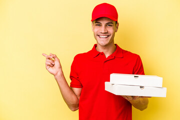 Young delivery caucasian man holding pizzas isolated on yellow background smiling and pointing aside, showing something at blank space.
