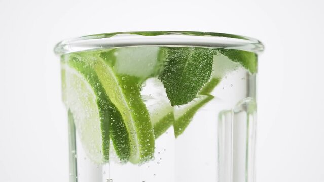 Soda water with lime, mint and ice in the glass on the white background, rotate, close up, 4k. Fresh lime detox water with bubbles.