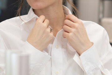 Young woman adjusts the collar of white blouse standing in front of mirror