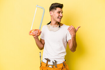Young electrician caucasian man isolated on yellow background.points with thumb finger away, laughing and carefree.