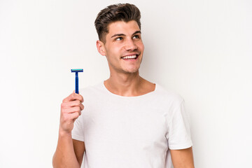 Young caucasian man shaving his beard isolated on white background dreaming of achieving goals and...