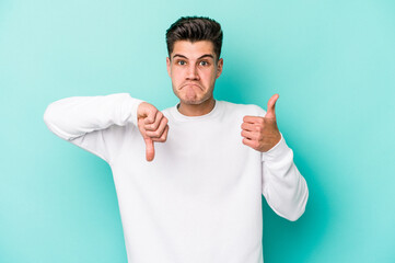 Young caucasian man isolated on blue background showing thumbs up and thumbs down, difficult choose...