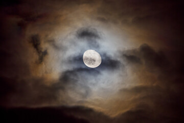 Mystery spooky moon shining through a clouds, glowing colorful moon halo