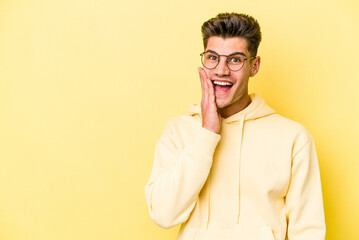 Young caucasian man isolated on yellow background shouts loud, keeps eyes opened and hands tense.