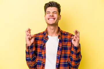 Young caucasian man isolated on yellow background crossing fingers for having luck