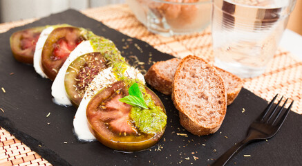 caprese salad with mozzarella, black tomatoes and pesto on black stone plate