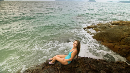Handsome long-haired woman chill relax resting on rock of sea reef stone, stormy cloudy ocean....