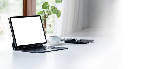 Blank white screen tablet with magic keyboard in modern office room.