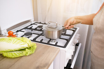 Fototapeta na wymiar Woman puts stainless steel pot on gas stove in modern kitchen. Cooking utensils concept
