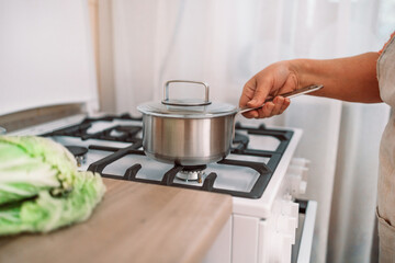 Woman puts stainless steel pot on gas stove in modern kitchen. Cooking utensils concept