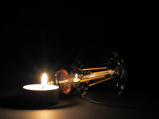Candle burning next to a lightbulb. Concept of rising energy costs, poverty, and energy shortages