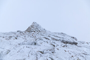 A scenic view of a frozen and snowy mountain summit peak in the Scottish mountain during a snow storm	
