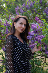 A beautiful girl of model appearance in a summer dress in a blooming garden among the aromas of bright lilac on a summer day.