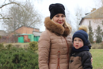 Mom and her little son are walking down the street in the countryside in winter. A little boy in a warm jacket and a winter hat