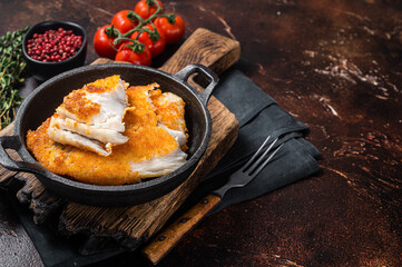 Roasted tilapia fillet in a skillet with breadcrumbs. Dark background. Top view. Copy space
