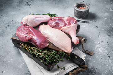 Butchered whole duck, raw breast steak, legs, wings on a butcher cutting board. Gray background. Top view