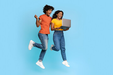 Emotional black man and woman with laptop jumping up