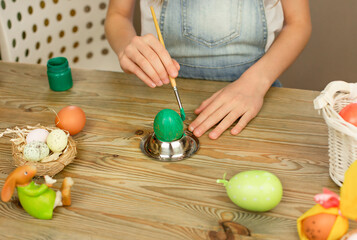 Brush for drawing in the hands of a child. Decorating Easter eggs. Preparation for Easter. On a wooden table there is a toy rabbit, eggs, paint.