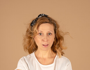 Studio portrait of a red-haired curly-haired surprised woman on a beige monochrome background